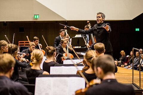 Das HTWK Orchester beim Spielen im Gewandhaus. Man sieht den Dirigenten.