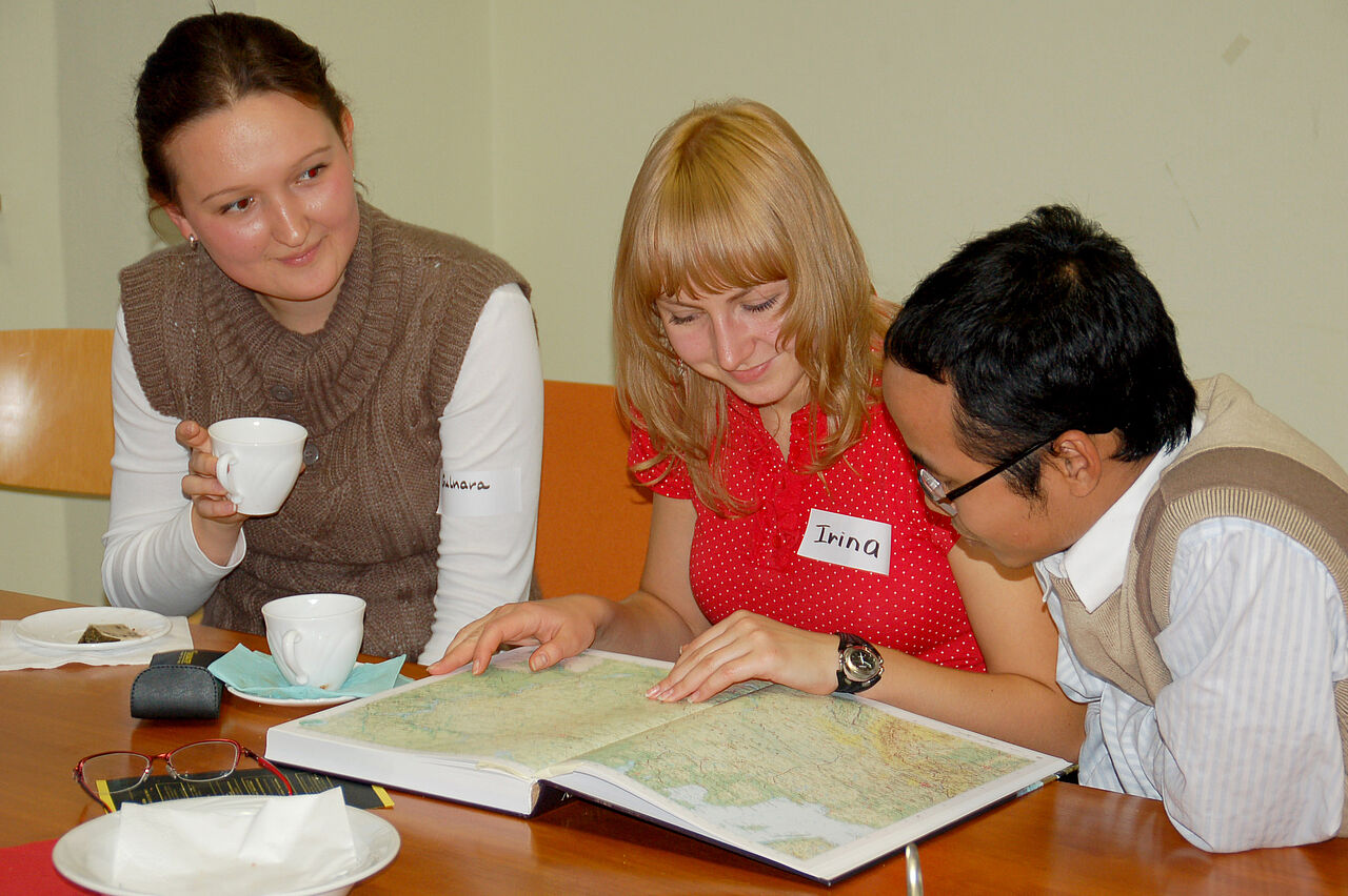 Drei Studierende schauen gemeinsam in einen Atlas