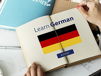 Buch "Learn German" mit deutscher Flagge. Offenes Buch mit Überschrift "Learn German" und einer deutschen Flagge
