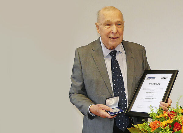 Dr. Staude festlich gekleidet im Anzug mit einer Urkunde in der linken und der Albert-Geutebrück-Medaille in der rechten Hand.