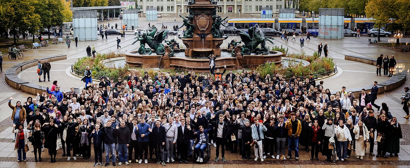Die Erstis 2025 große Menschengruppe auf Stadtplatz vor Obelisk und Brunnen mit Gebäuden im Hintergrund