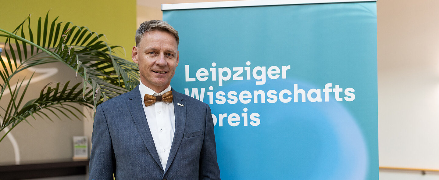 Prof. Alex Stahr Mann mit Urkunde steht vor Plakat