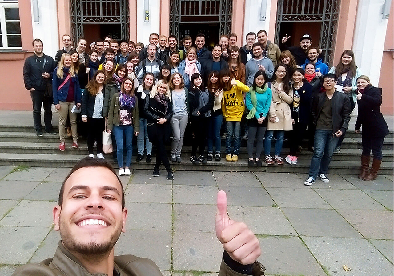 A male student takes a selfie with a group of students in front of the Lipsius building of the HTWK