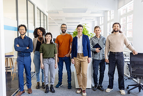International Career Office Eine multikulturelle Gruppe von jungen Erwachsenen steht in einem Büro und alle schauen frontal in die Kamera.