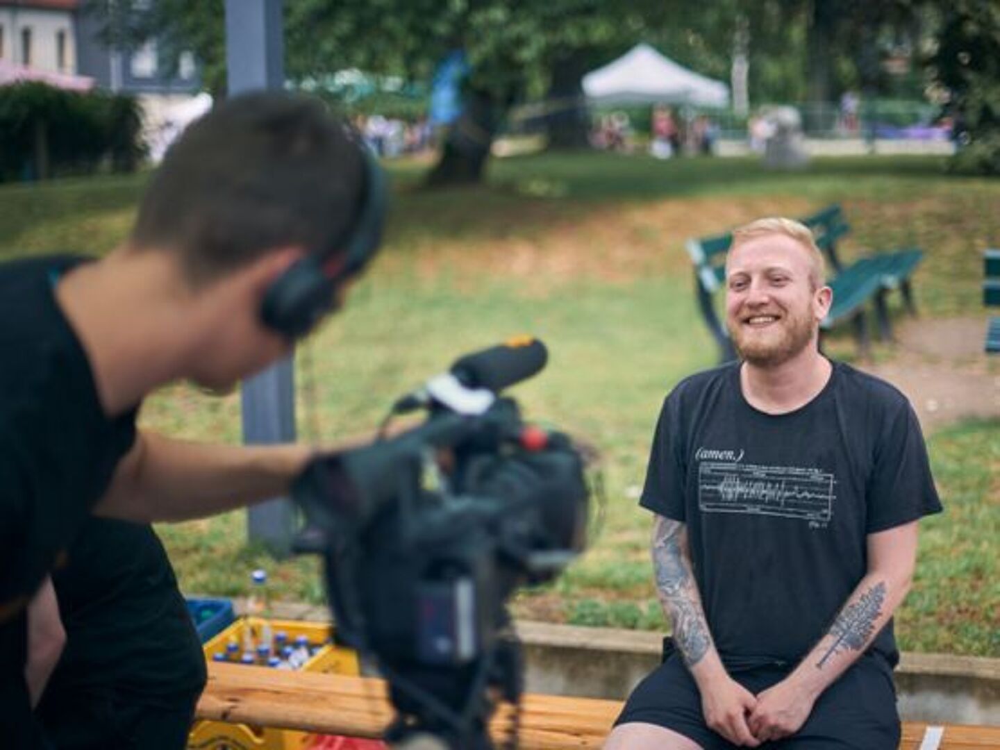 Es wird eine Interviewsituation dargestellt. Ein Kameramann steht mit einer Kamera vor einem Interviewpartner.