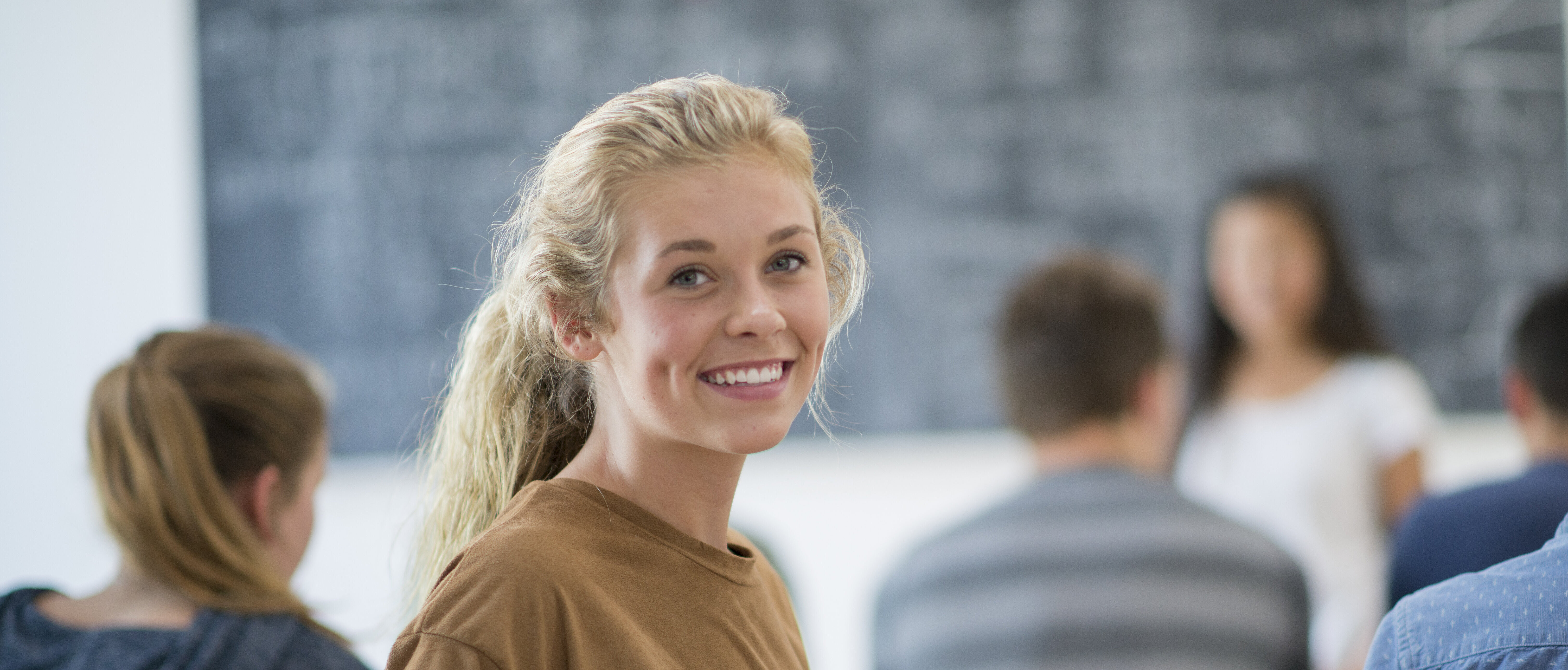 Bachelorstudiengang Betriebswirtschaftslehre Eine junge Frau sitzt in einer Vorlesung und dreht sich um und lächelt in die Kamera.