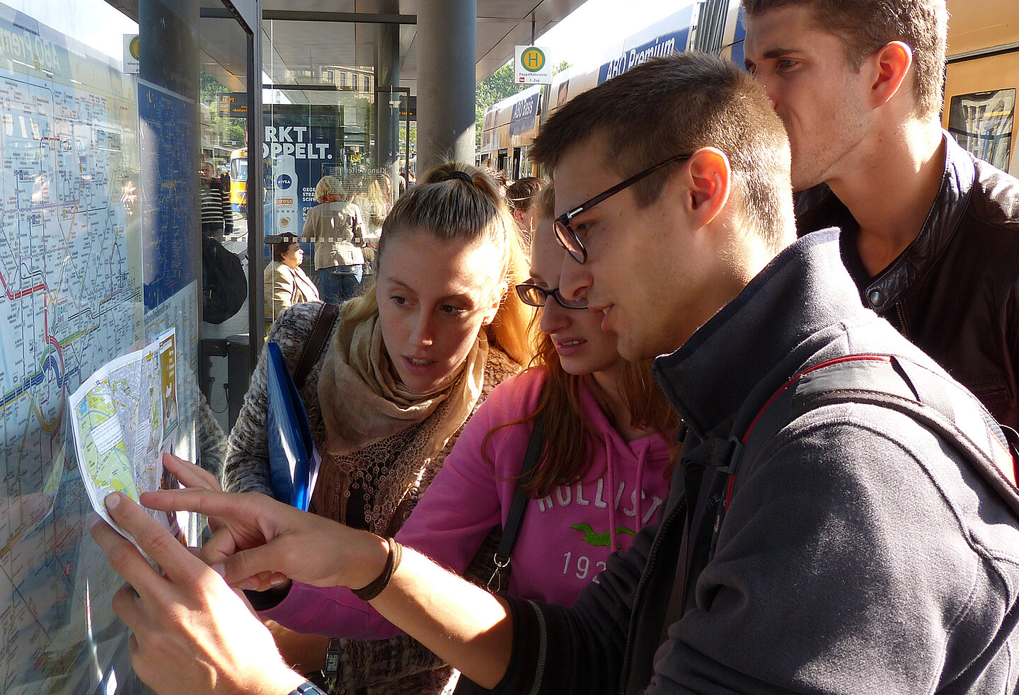 Ein Mentor erklärt einigen Studierenden an einer Haltestelle das Verkehrsnetz mit einer Karte