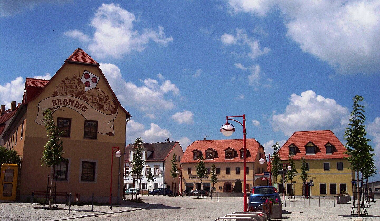 Blick auf den Marktplatz der Stadt Brandis im Sonnenschein, leicht bewölkter Himmel.