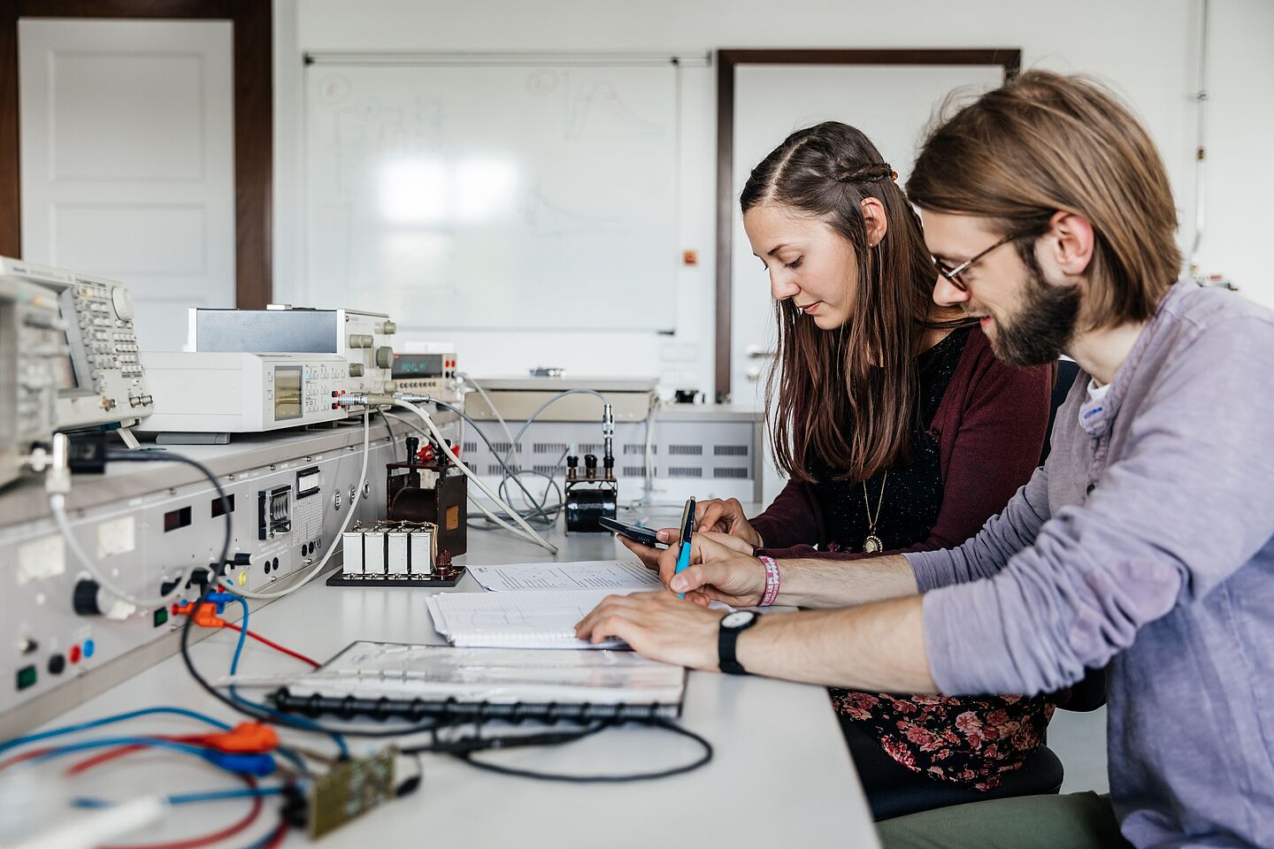 Two people working at a table full of electronics and cables