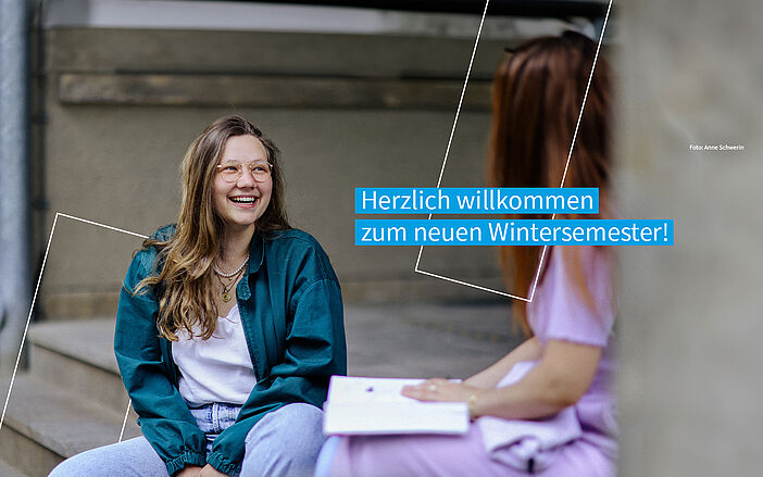 Studentin sitzt freudestrahlend im Trefftz-Bau Eingangsbereich und unterhält sich mit einer Kommilitonin. Auf dem Bild befindet sich der Text "Herzlich willkommen zum neuen Wintersemester!"