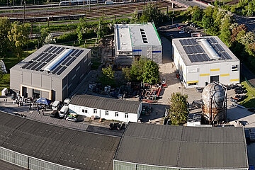 Campus Weigelstraße Drohnenaufnahme vom Campus mit mehrere großen Hallen in der Nähe von Wald und Schienen.