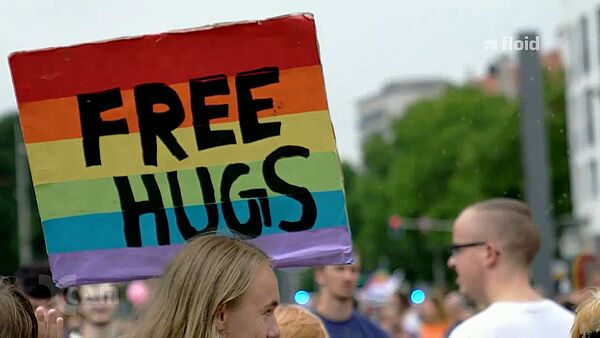 Screenshot einer Sendung von floid: ein Foto vom CSD, Menschen tragen ein Regenbogenplakat mit der Aufschrift Free Hugs