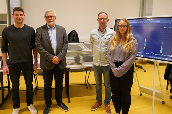 Gruppenfoto vor der Versuchsanlage Organic Photovoltaic mit großem Bildschirm im Hintergrund