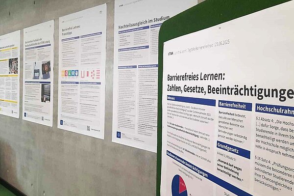 Posterausstellung  an einer grauen Betonwand sind Poster in Größe A0 in einer Reihe aufgehangen, im Vordergrund  ist das Poster mit dem Titel " Barrierefreies lernen: Zahlen, Gesetze, Beeinträchtigungen" zu sehen