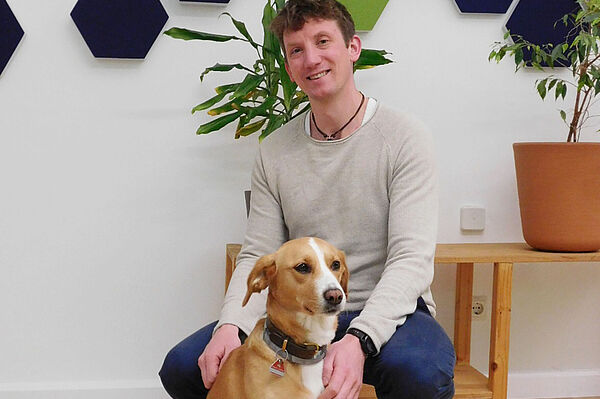 lorian Stegmann kniet lächelnd neben seinem Hund Pepper in einem Büro. Darunter steht der Text: 'Florian Stegmann mit seiner „Feelgood-Managerin“ Pepper.'