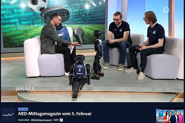 Felix Loos (re.) und Johannes Walter (mi.) von den HTWK Robots waren am 05.02.2026 mit zwei Robotern im "ARD-Mittagsmagazin" als Talkgäste zu Gast bei Tino Böttcher (li.). Im Fernsehstudio interagiert Moderator Tino Böttcher sichtlich begeistert mit einem der beiden HTWK Roboten im Gespräch mit Felix Loos und Johannes Walter.
