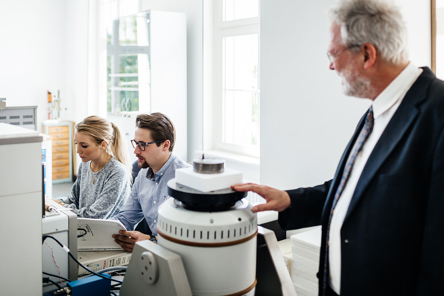 In the foreground, a professor looking at two younger researchers in the background