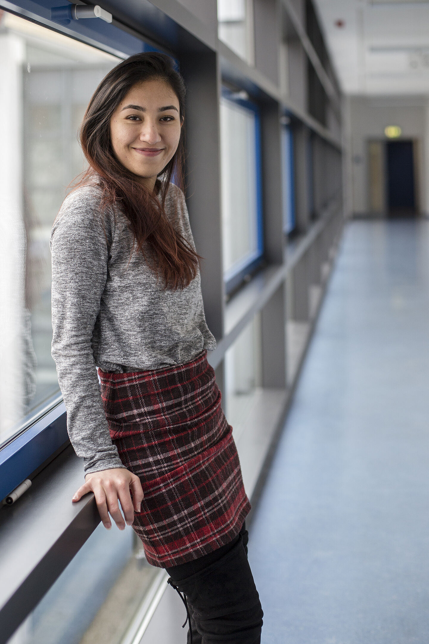 Elaha Fakhri steht in einem Gang der HTWK Leipzig und lehnt an einer Fensterbank. Sie blickt lächelnd in die Kamera.