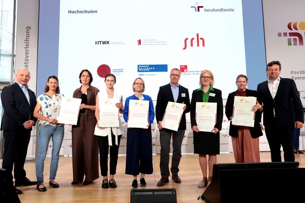 HTWK-Kanzlerin Prof.in Swantje Rother (3. v. re.) mit dem Zertifikat auf der Festveranstaltung. (Foto: Jens Schicke/ berufundfamilie Service GmbH) Gruppe von Menschen mit Urkunden auf einer Bühne