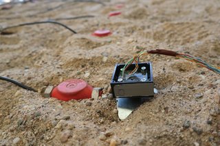 SIMPeL Kleiner Sensor mit Kabeln liegt im Sand; daneben rote Messpunkte