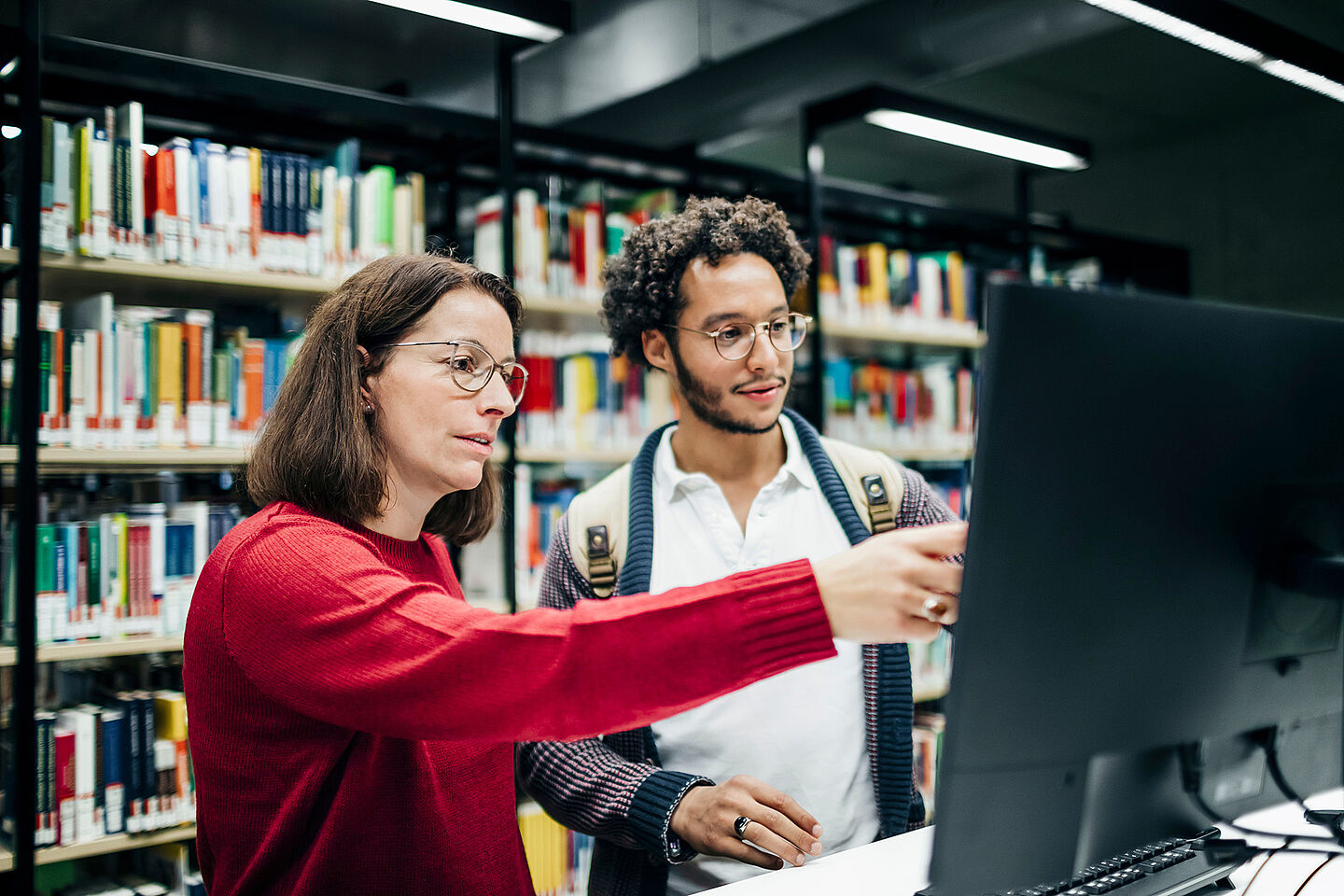 Eine Frau zeigt einem Studenten etwas am Bildschirm.