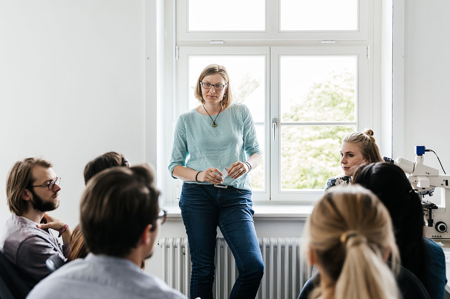 Group of students sits in front of a professor and listen to her