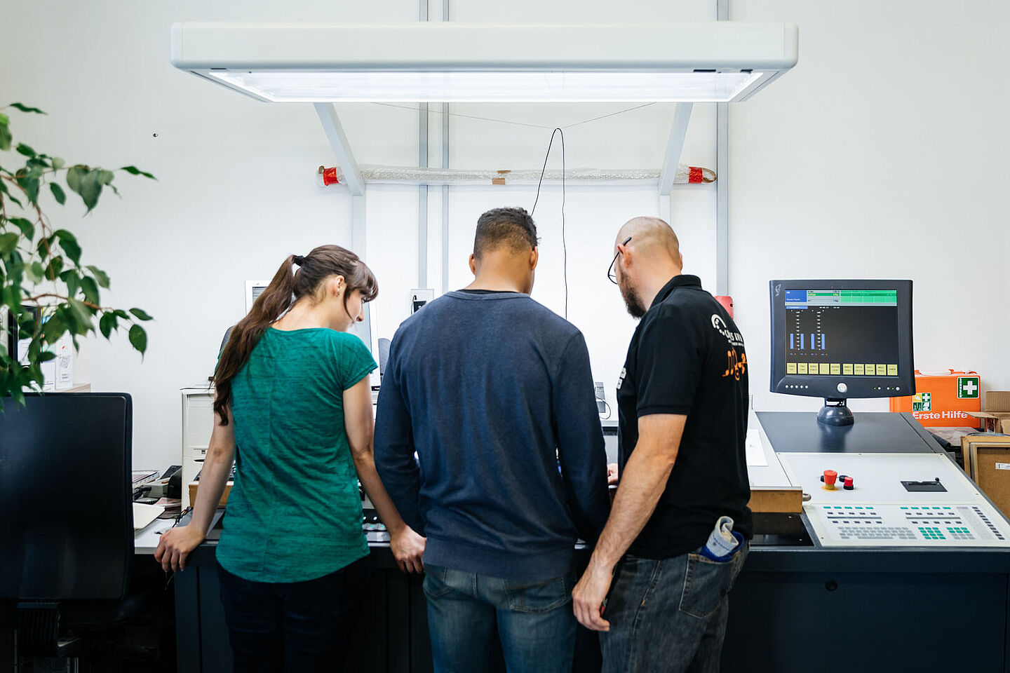 Three people from behind at a large printing press