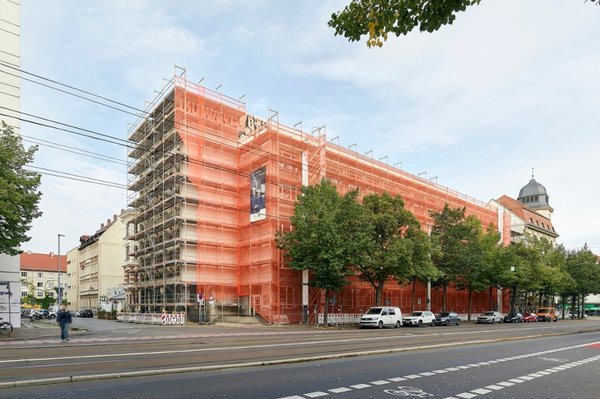 Fassadengerüst am Geutebrück-Bau der HTWK Leipzig. (Foto: Michael Moser/SIB) Eingerüstetes Gebäude mit orangen Planen an großer Straße