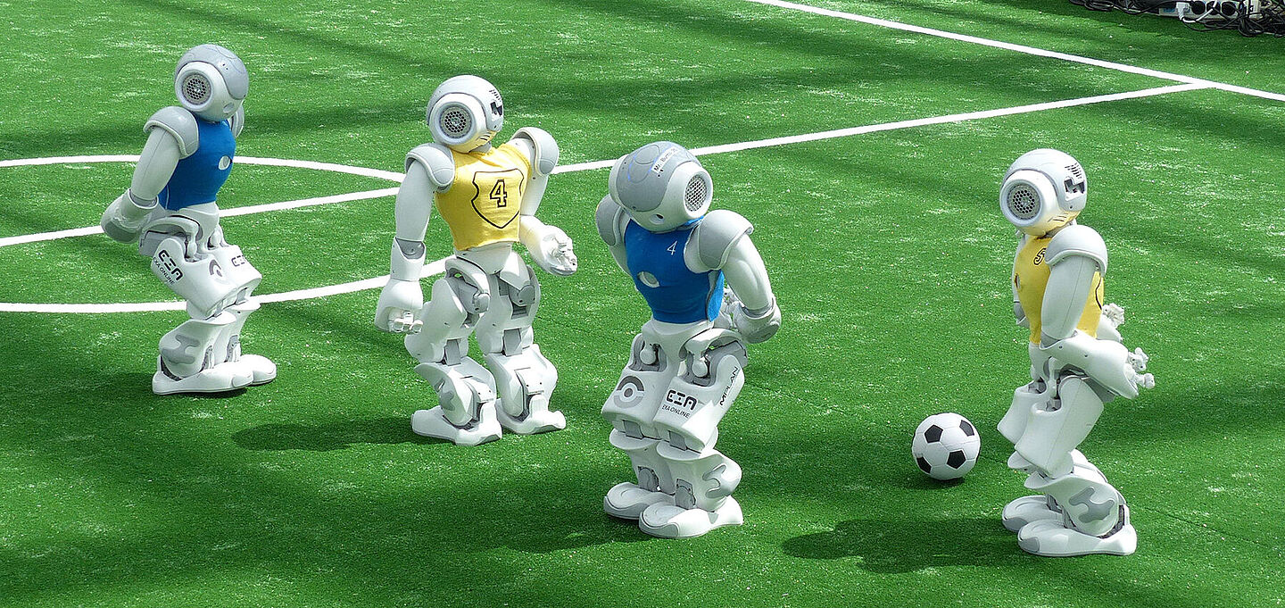 Vier kleine Roboter spielen Fußball auf einem eigens für sie konzipierten Spielfeld