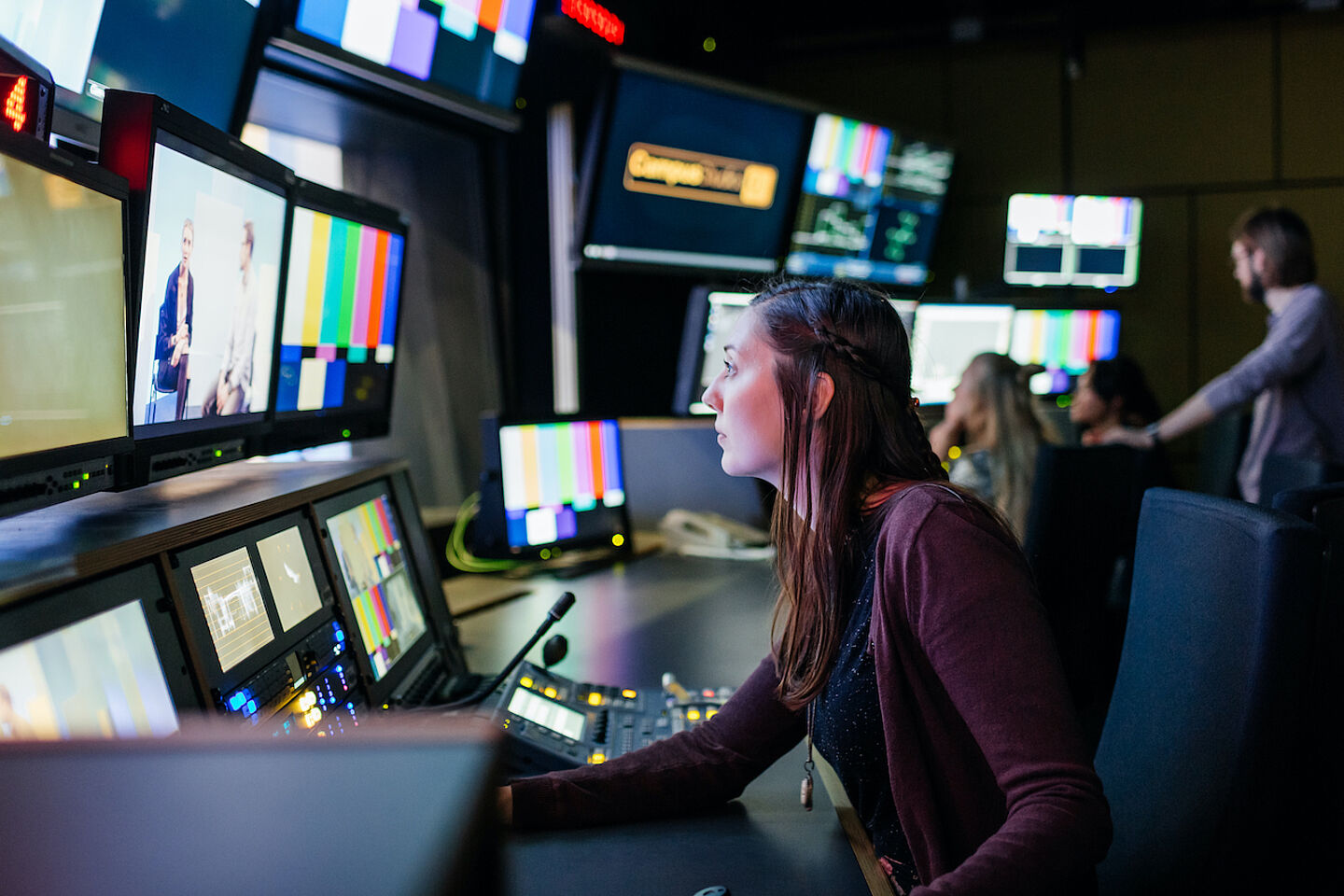 Student sitting in the campus studio in front of a wall full of monitors