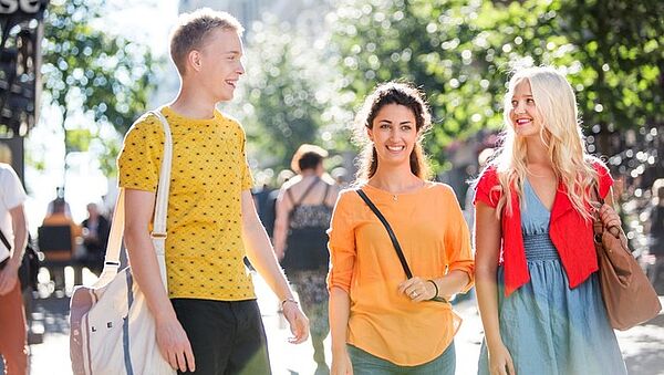 Drei Studierende bei Sonnenschein auf einem Campus