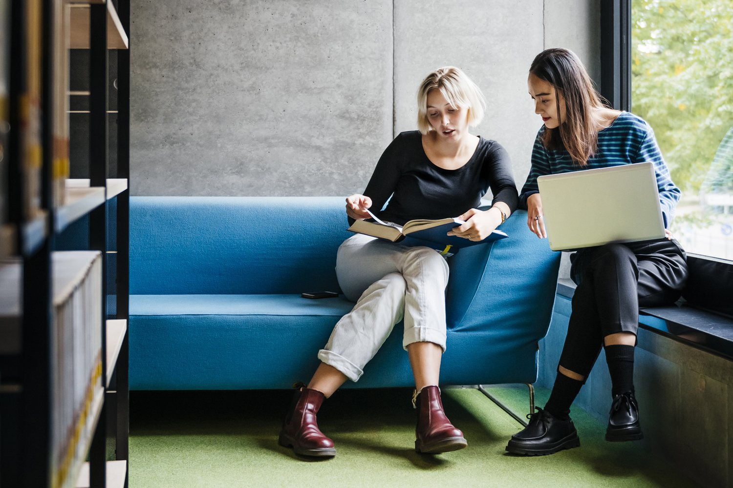 Mentoring unter Studierenden Zwei Studierende gehen gemeinsam Studienmaterial in der Bibliothek durch.