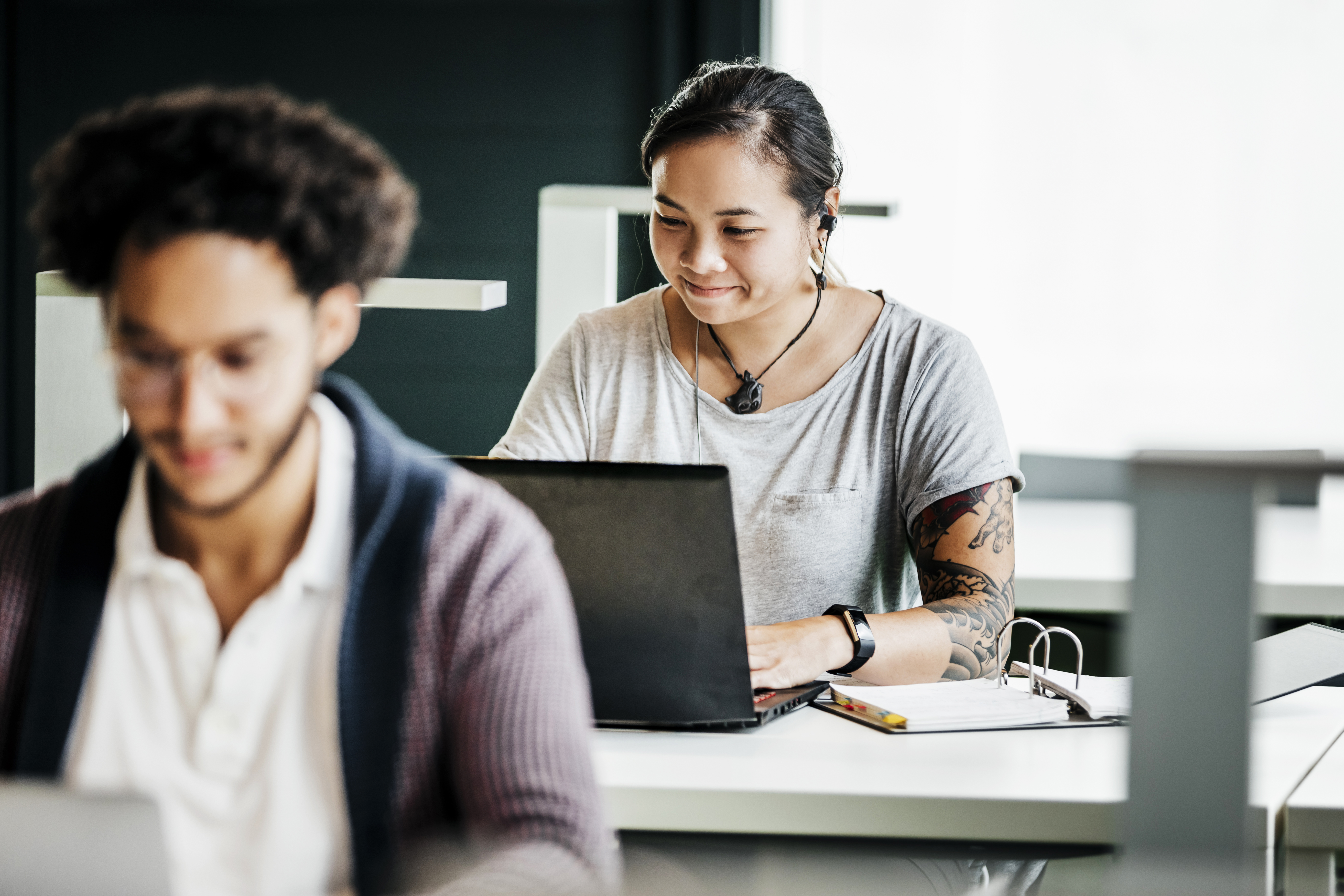 Studierende beim Arbeiten Zwei Studierende sitzen jeweils vor ihrem Laptop an Arbeitstischen.