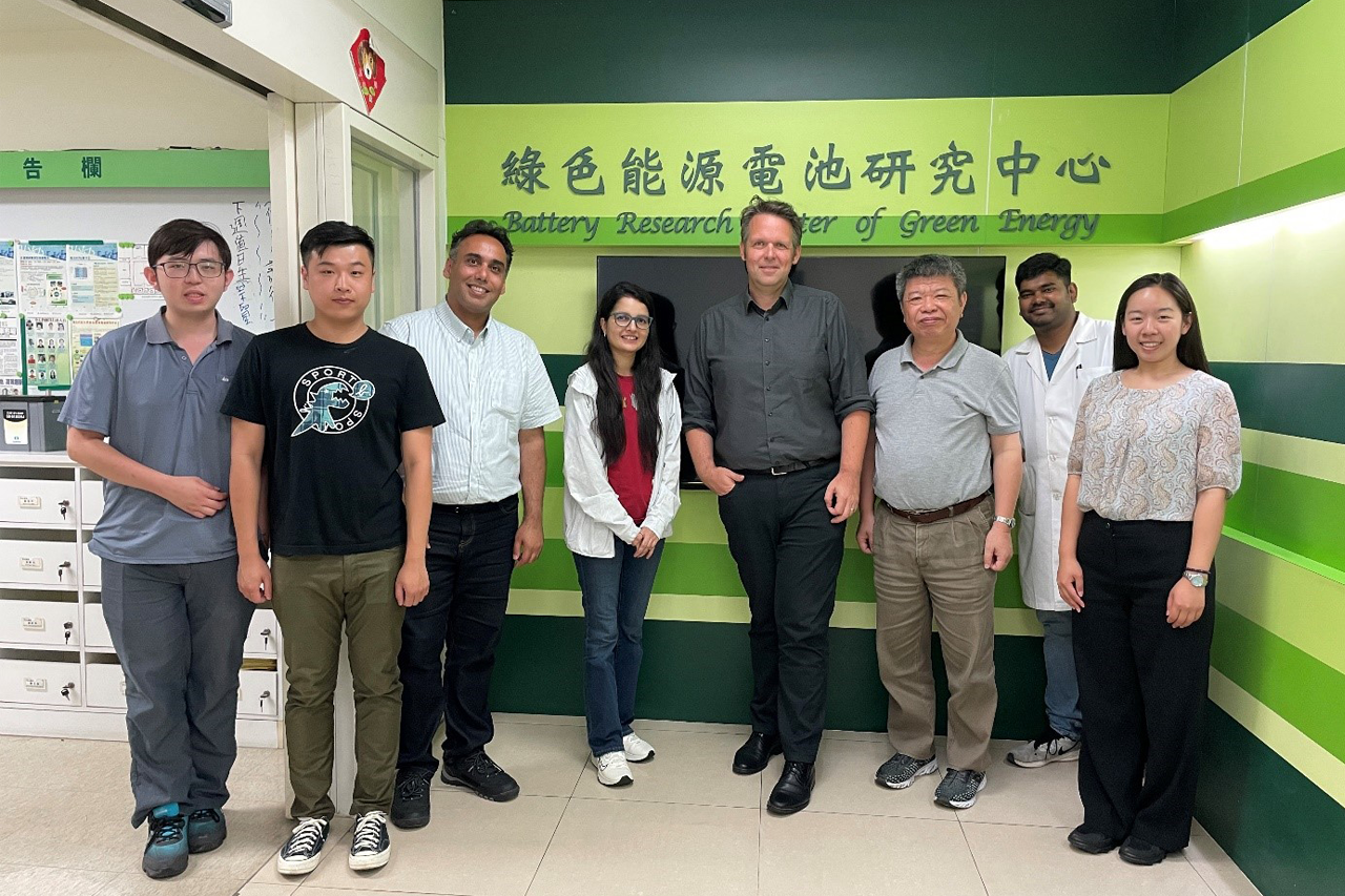 Gruppenfoto von Prof. Böhm und Team mit Wissenschaftlerinnen und Wissenschaftlern der MCUT in Taiwan, alle lächeln in die Kamera, Logo MCUT im Hintergrund