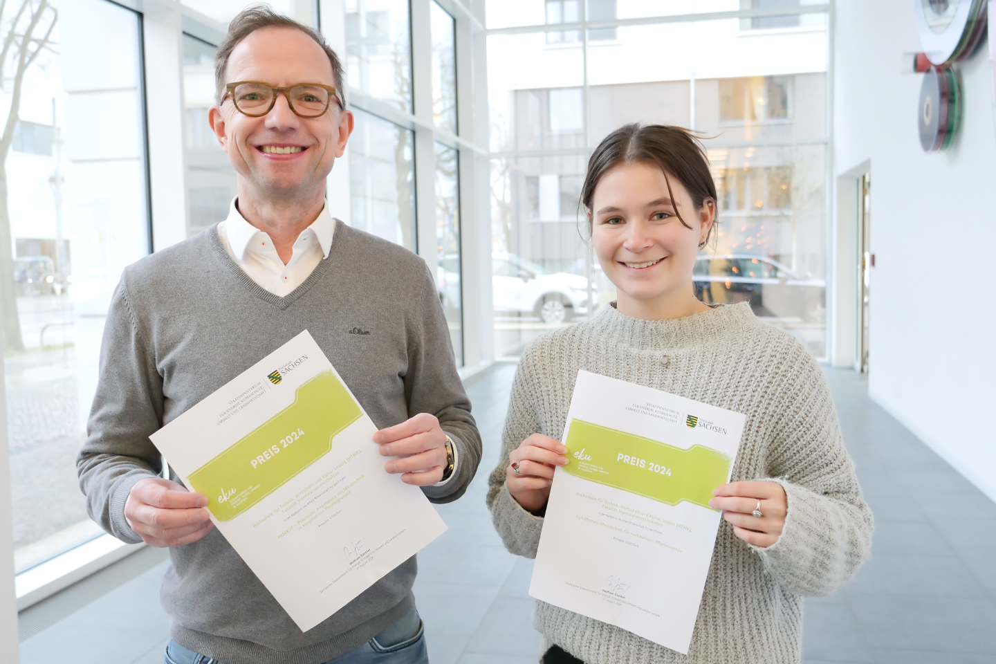 Portraitaufnahme von Prof. Rudoph und Elena Richter mit Urkunden in der Hand