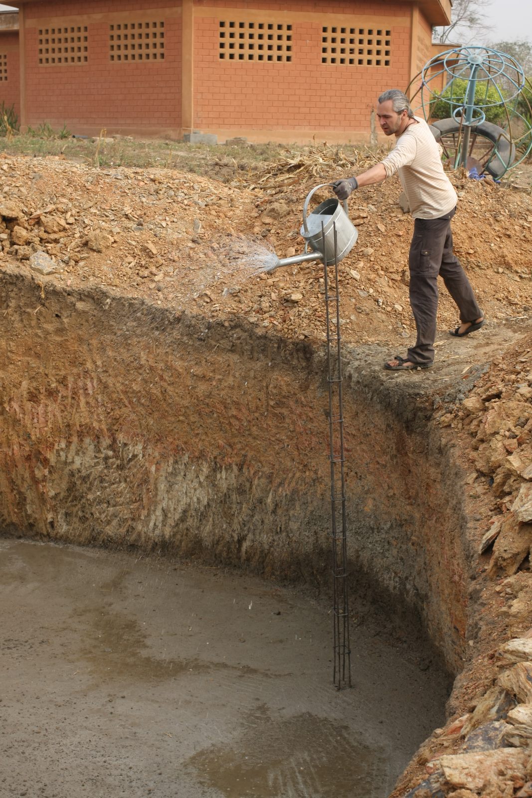 Der deutsche Ingenieur steht am Rand der Grube und gießt mit einer Kanne Wasser in dieselbe.