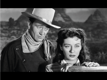 Ein Cowboy mit Hut und Halstuch schaut auf eine Frau hinab, die in die Ferne sieht.
