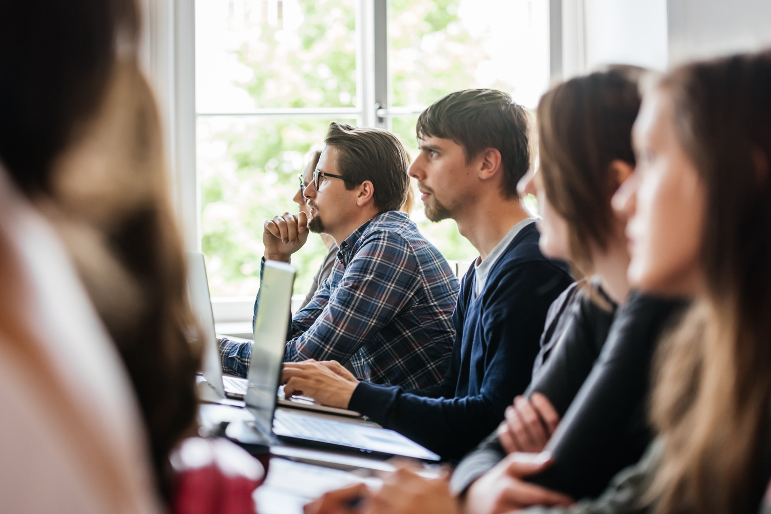 Studieren an der HTWK Leipzig Mehrere Studierende in einem Seminarraum, dabei ist ein Student besonders fokussiert, während die anderen unscharf dargestellt sind.